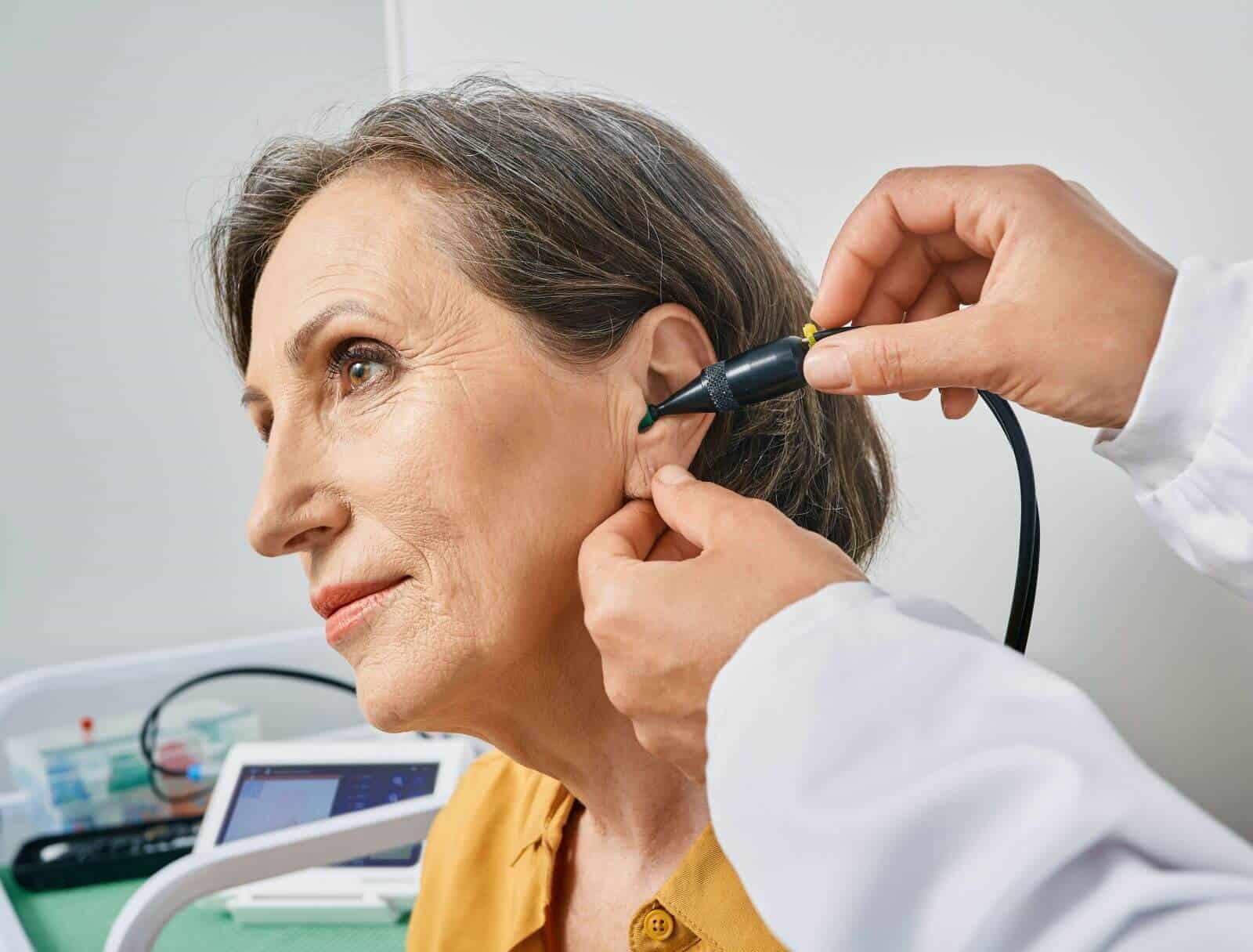 audiologist conducting ear exam of woman as she looks onward