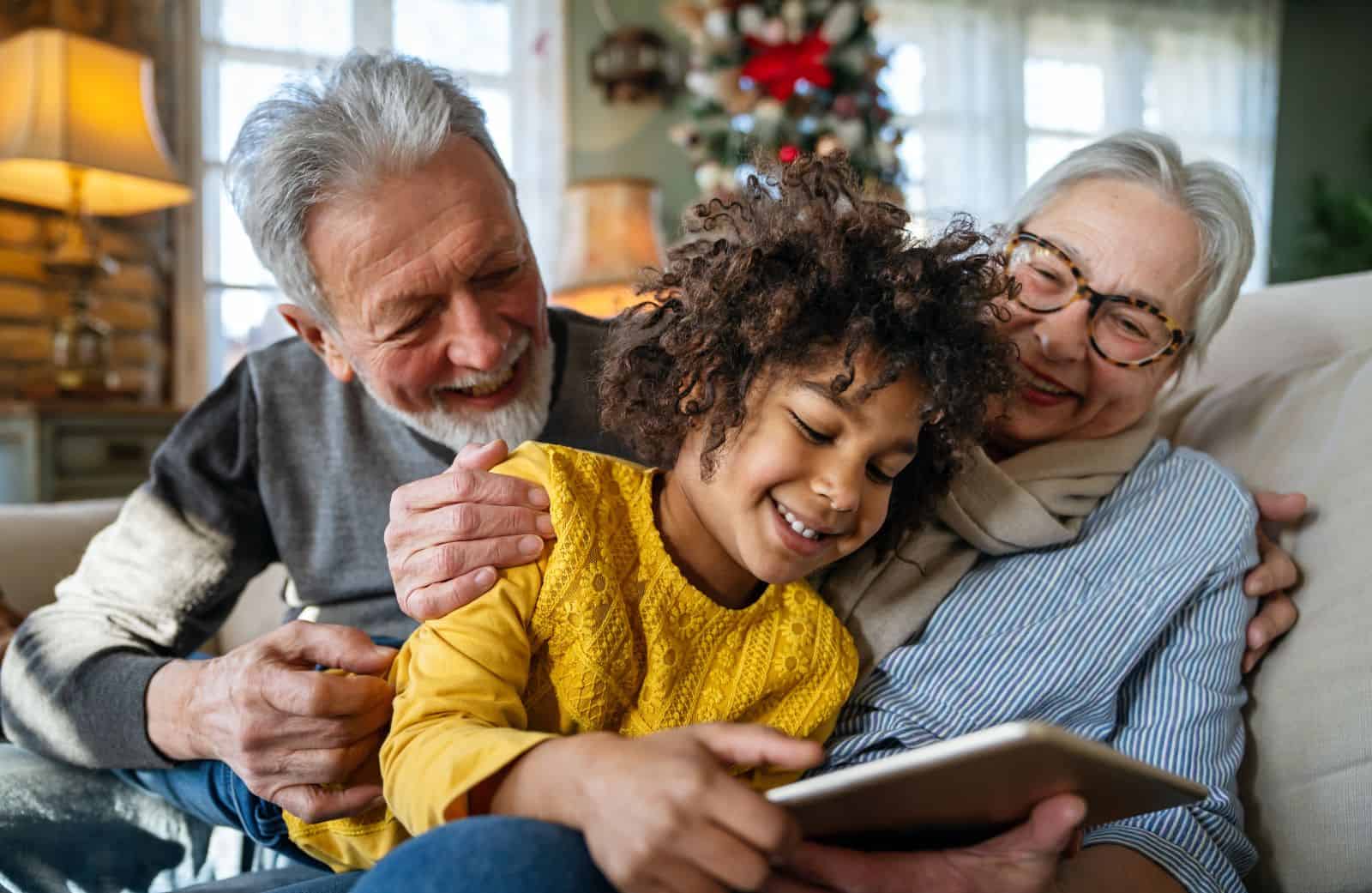 grandparents holding grandchild as he plays on tablet