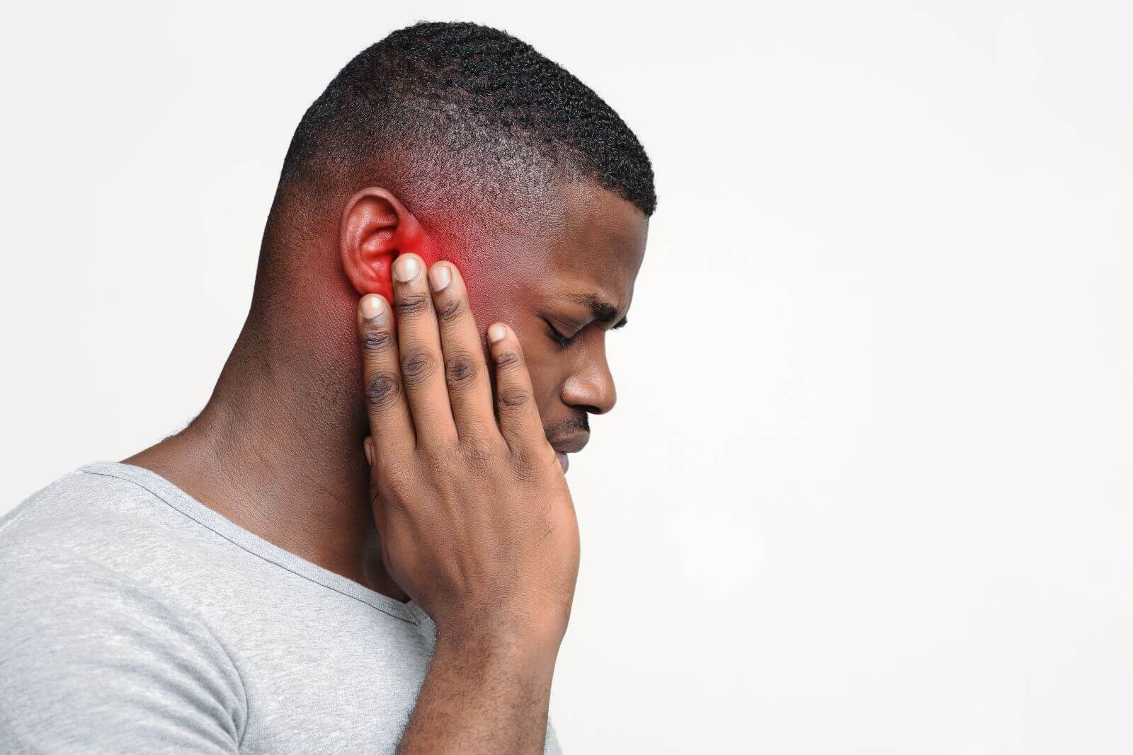 man grabs ear, ear is red indicating pain.